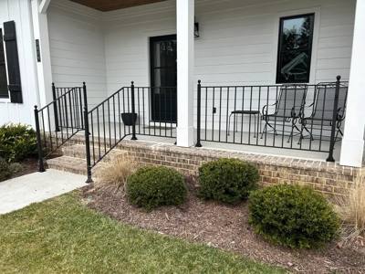 Black picket railing enclosing a white-columned porch above clipped shrubs