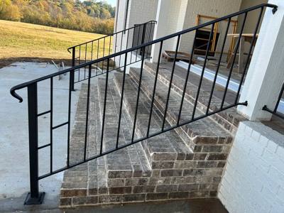 Black picket railing following brick porch stairs beside white columns