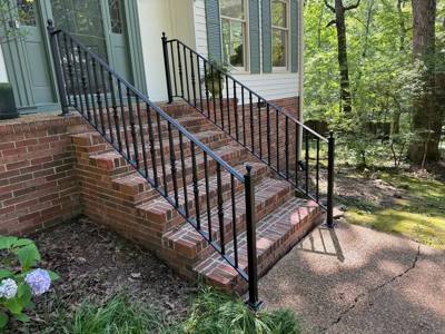 Black picket railings beside brick stairs descending toward a wooded yard