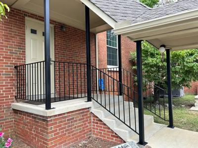Black picket railings framing a small concrete entrance landing at a brick house