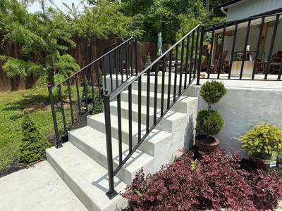 Black picket railings on pale concrete steps beside manicured shrubs
