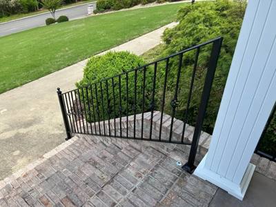 Black picket stair railing beside brick paving and a white porch column