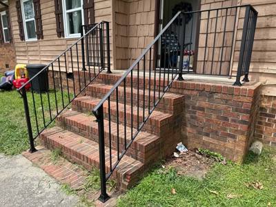 Black picket stair railings leading to a covered entrance at a brown-sided house
