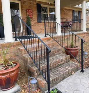 Black porch and stair railings beside white columns and a stone wall