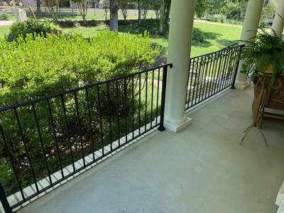 Black porch railing between pale columns above a green hedge