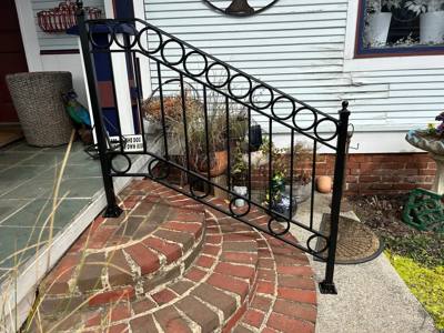 Black porch railing with circular motifs above curved brick paving