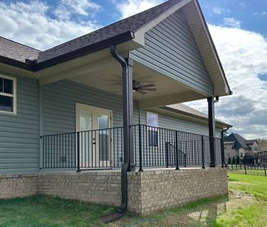 Black porch railings above a brick foundation beneath a gabled roof