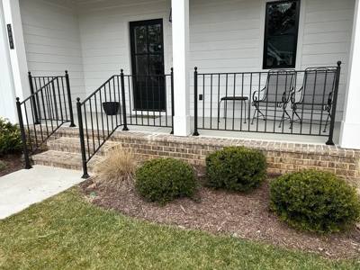 Black porch railings around a small white entry with outdoor chairs