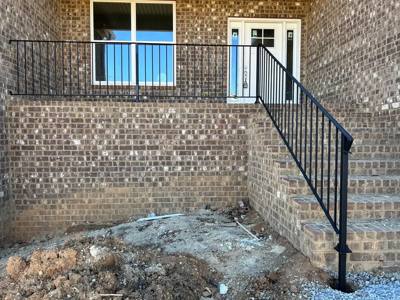 Black railing around a raised brick landing and concrete steps