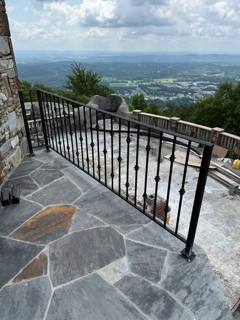 Black railing around a stone terrace overlooking distant hills