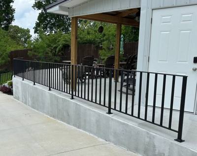 Black railing bordering a covered patio beside a concrete driveway