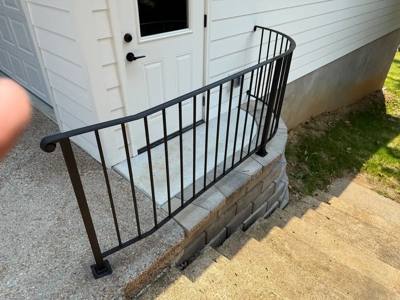 Black railing curving around a small brick entry platform