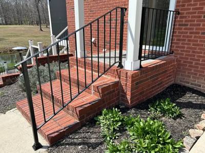 Black railing following sloping brick porch steps beside white columns