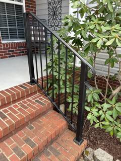 Black railing on brick entry steps beside flowering greenery