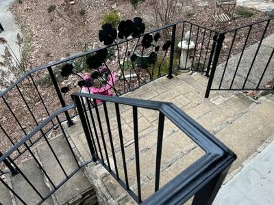 Black railing with sculpted flower panels overlooking stone garden steps