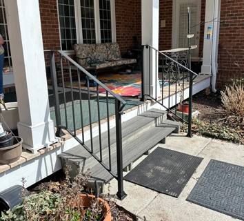 Black railings around a small white-columned porch with gray steps