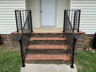 Black railings around brick steps and a small landing at a white-sided house