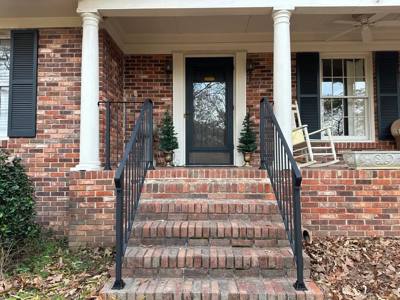 Black railings beside brick steps leading to a columned front porch