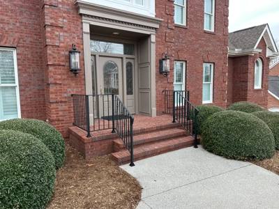 Black railings bordering brick steps at a large arched double-door entrance