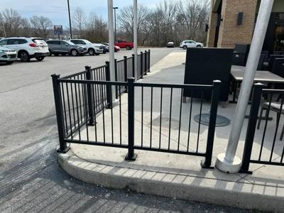 Black railings enclosing a paved outdoor seating area beside a parking lot