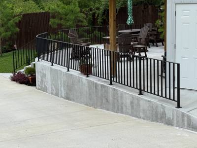 Black railings enclosing a raised concrete patio with outdoor furniture