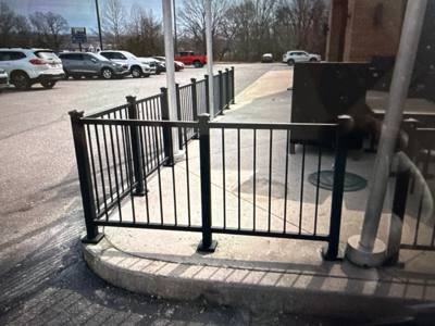Black railings enclosing an outdoor seating area beside a parking lot