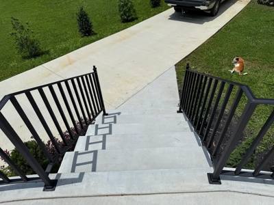 Black railings flanking concrete entrance steps viewed down toward a driveway