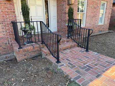 Black railings framing a small brick stoop and paved entrance path