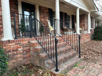 Black railings framing brick porch steps below a row of white columns