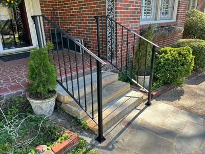 Black railings framing small entrance steps between brick walls and shrubs