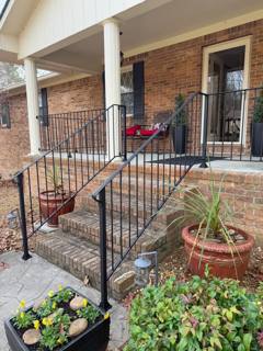 Black railings on stone steps leading to a covered brick porch