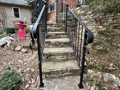 Black railings with curled ends along narrow stone garden stairs