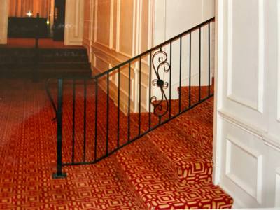 Black scroll-accent stair balustrade beside patterned red carpet