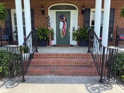 Black scroll-end railings flanking a brick porch beneath white columns
