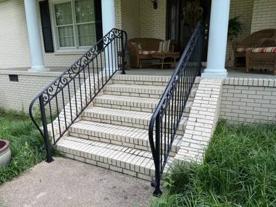 Black scrollwork railings flanking wide pale brick porch steps