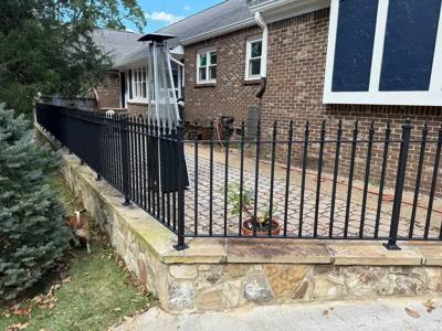 Black spear-top fence mounted along a low stone wall beside a brick house