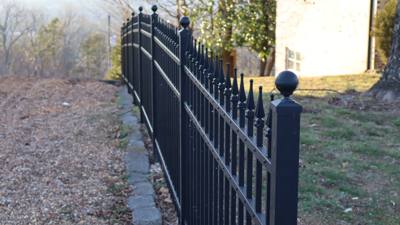 Black spear-top fence with ball-capped posts along a wooded boundary
