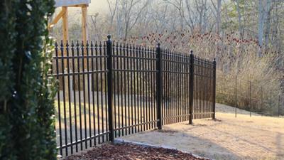 Black spear-top gate beside a paved drive and wooded slope