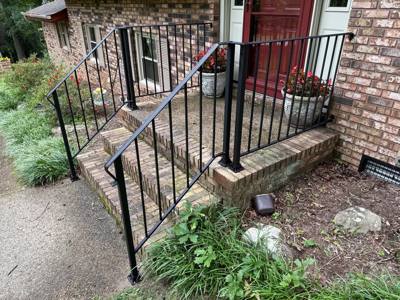 Black stair and landing railings at a stone-faced front entrance