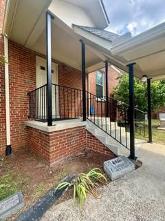 Black stair railing rising to a covered brick front porch