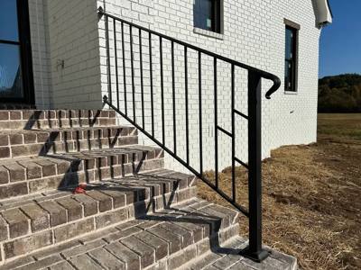 Black stair railing with a returned handrail beside brick steps