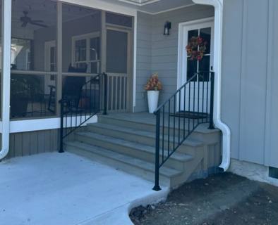 Black stair railings at a gray concrete porch beside a screened patio