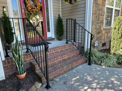 Black stair railings beside brick porch steps and tall potted plants