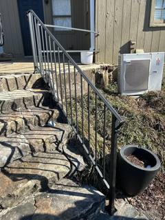 Black stair railings beside rough stone steps and an outdoor air-conditioning unit