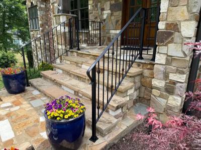 Black stair railings beside stone entry steps and flower pots