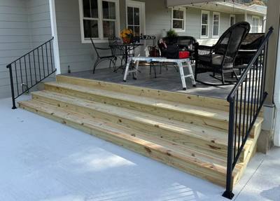 Black stair railings flanking broad wooden steps to a furnished porch