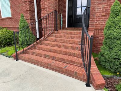 Black stair railings with rounded returns at a brick doorway