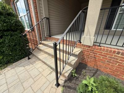 Black vertical-bar handrails on concrete steps beside a brick porch