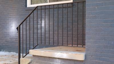 Black vertical-bar railing along steps against a painted brick wall