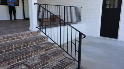 Black vertical-bar railing beside brick front steps and a covered porch